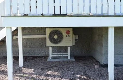 Luft-luftvärmepumpens utedel placerad på ett stativ dolt under husets uteplats